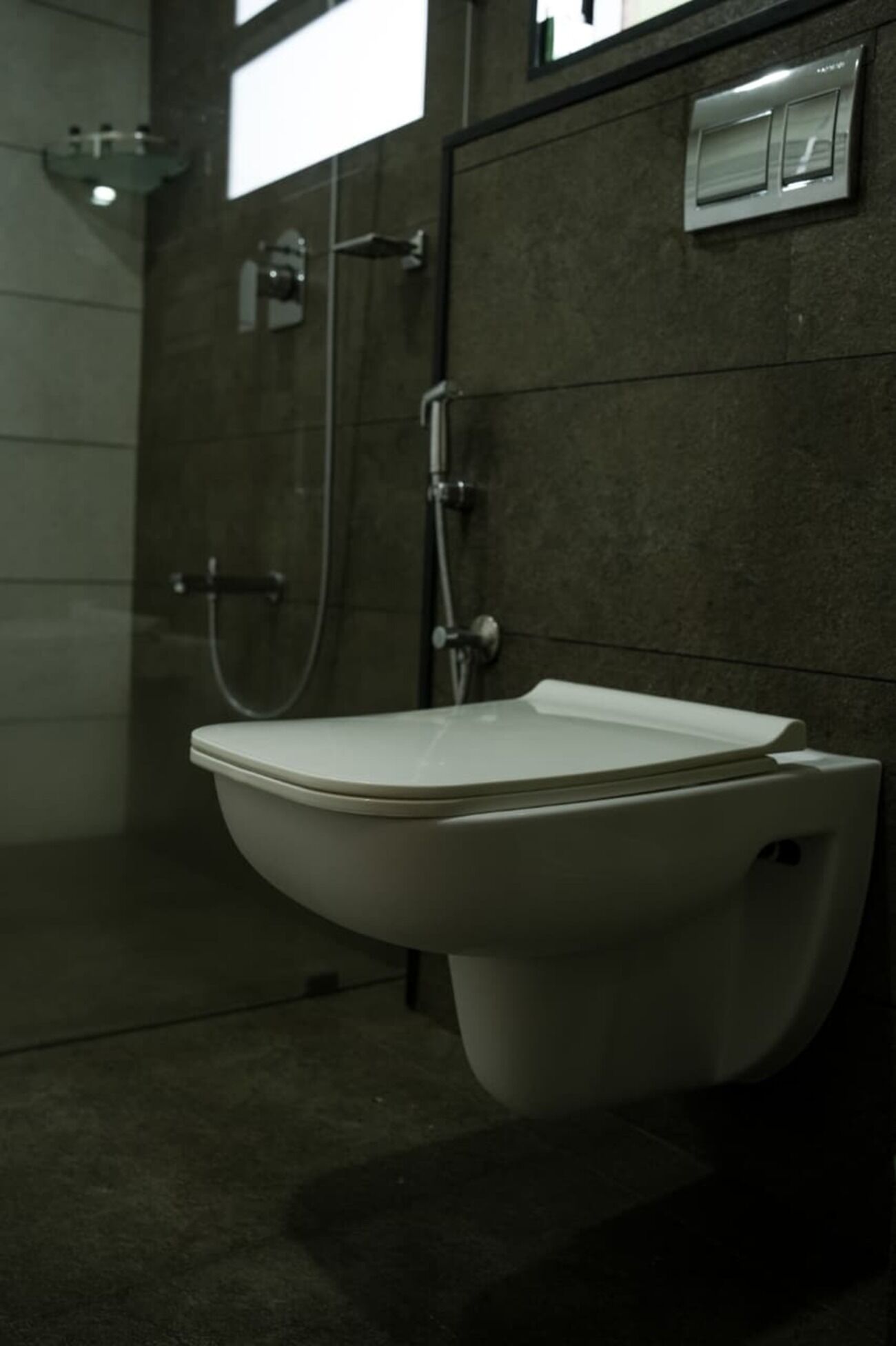 Une salle de bain moderne avec des toilettes suspendues, un espace douche et une petite étagère.