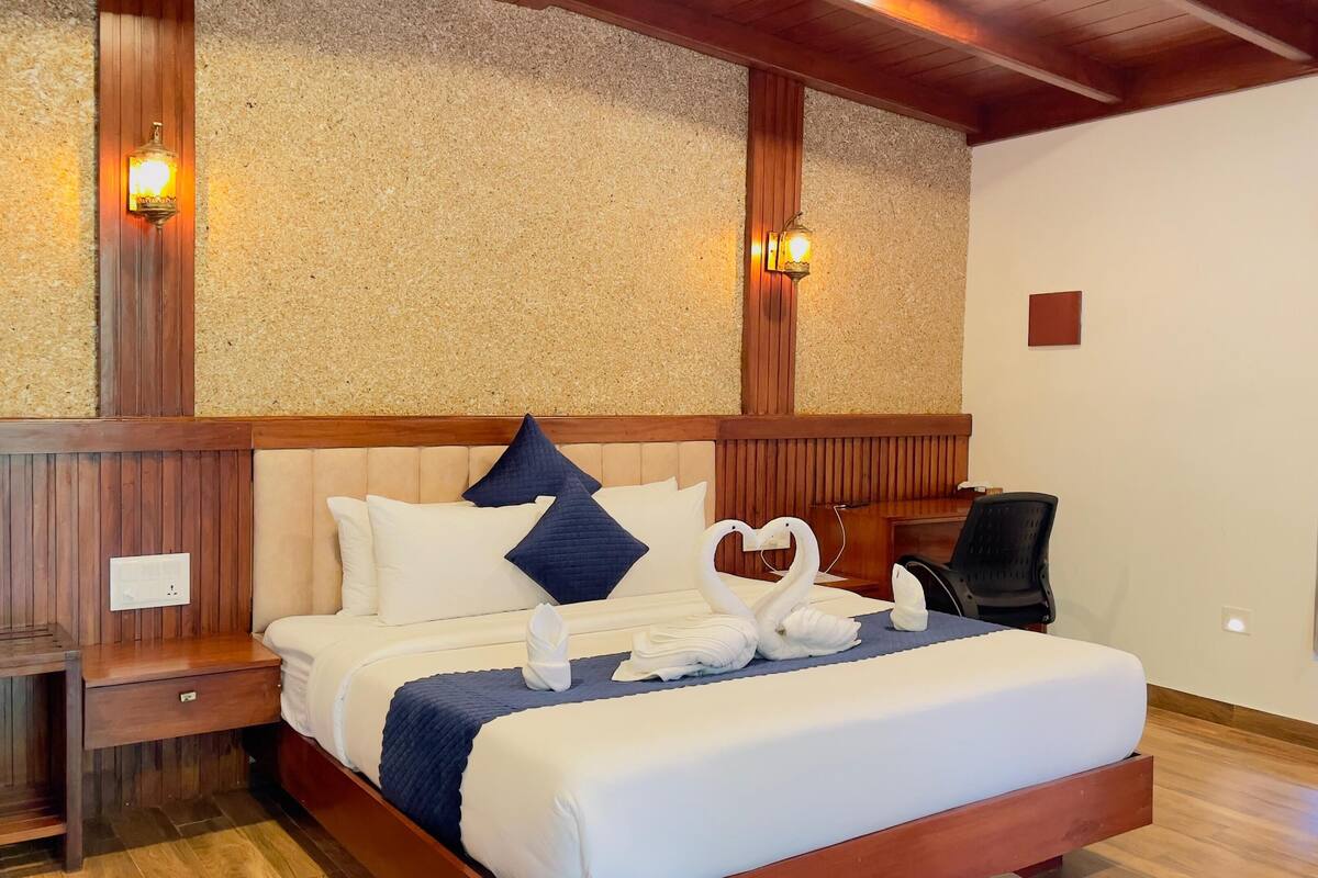 Un lit bien fait, agrémenté d’une décoration en forme de cœur réalisée avec des serviettes, d’une tête de lit en bois et de deux lampes fixées au mur.