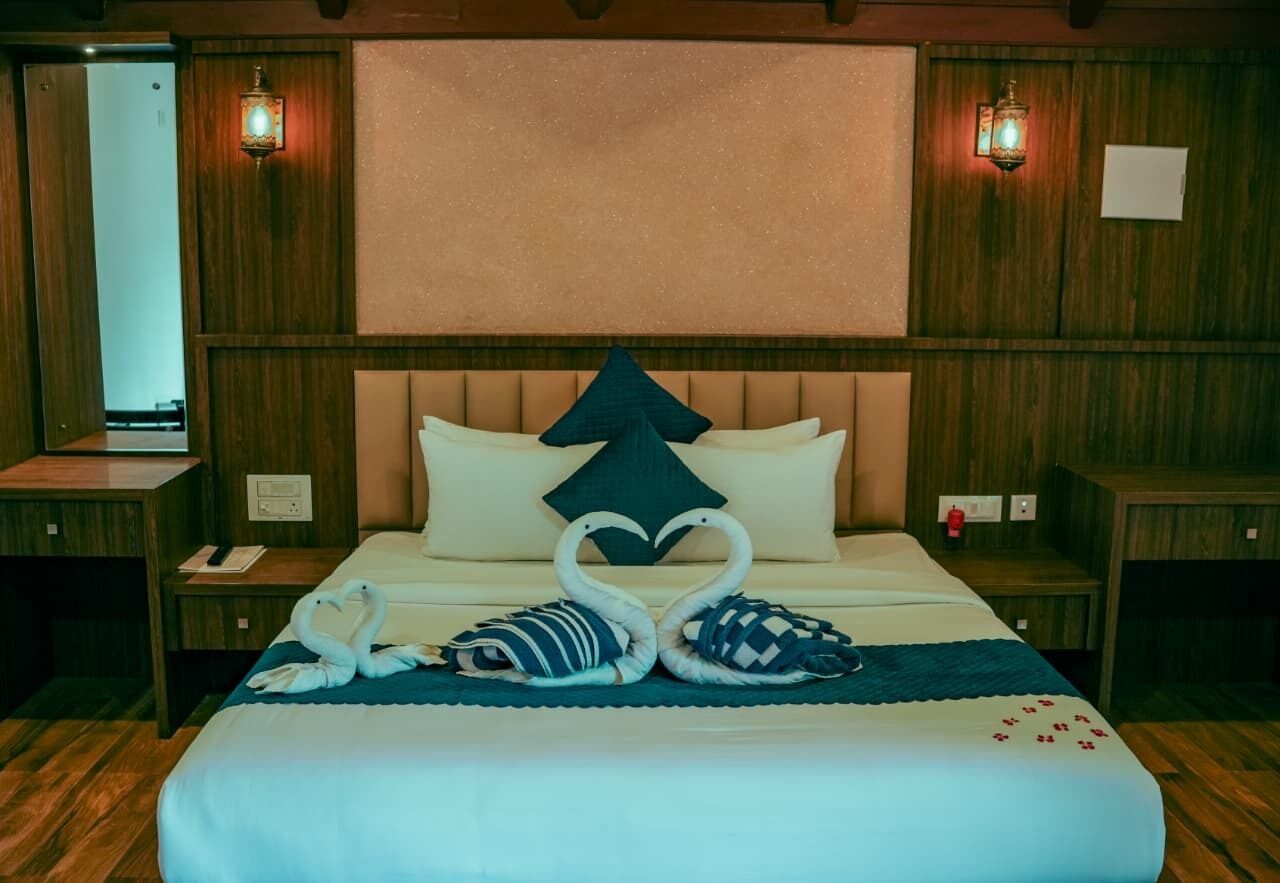 A hotel room with a large bed, wooden paneling, two nightstands, a mirror, and wall-mounted lamps.