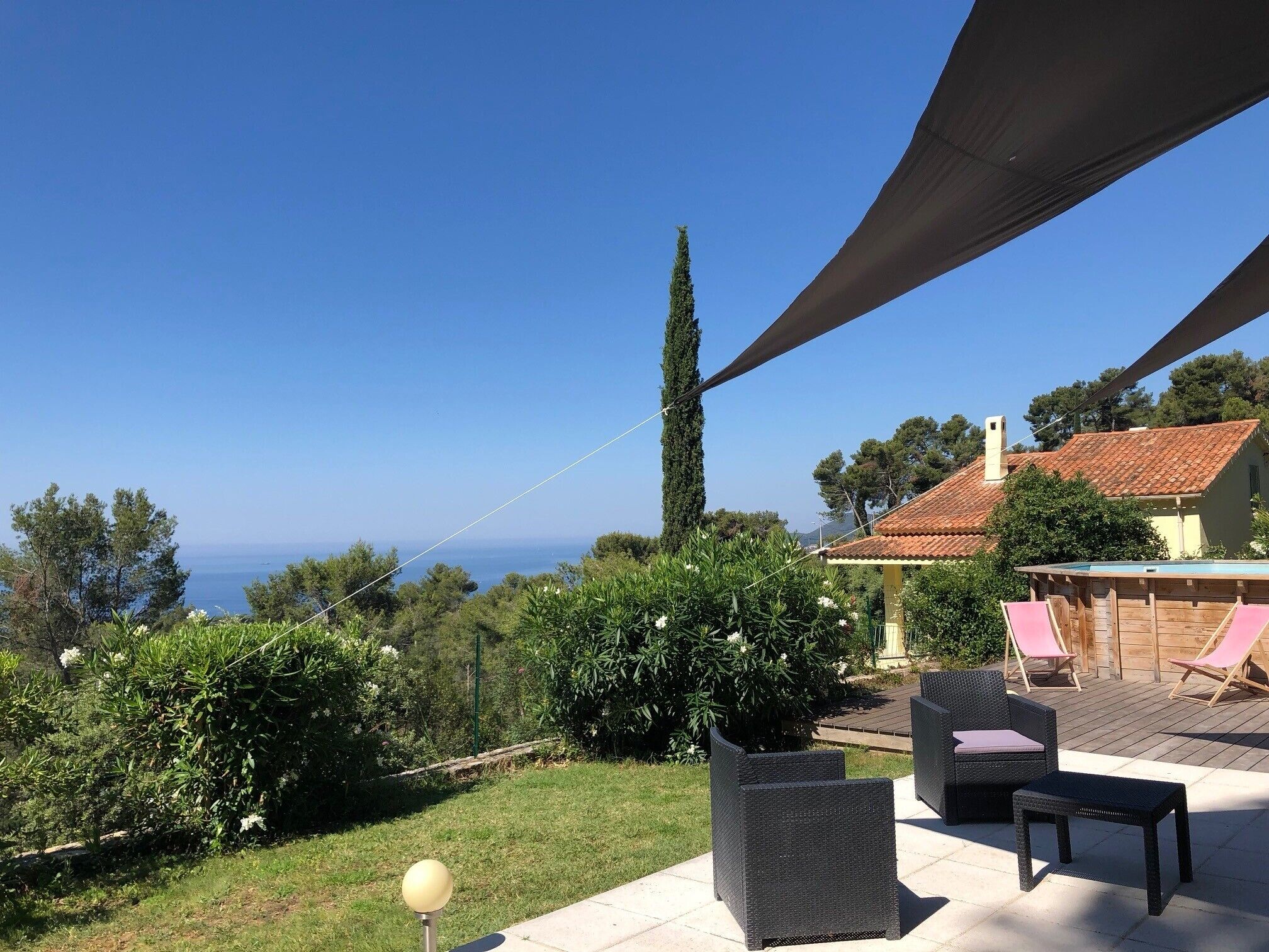 Un espace patio aménagé avec du mobilier d’extérieur, une vue sur la mer et un grand arbre.