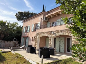 Un bâtiment à deux étages doté d’une façade en pierre, d’un balcon avec des balustrades en métal et d’une terrasse pavée aménagée avec du mobilier d’extérieur.