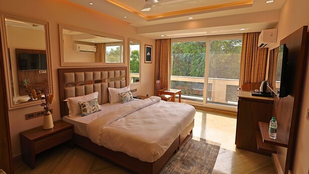 A spacious bedroom with a large bed, a bedside table, a chair, a desk, and a television. - FlxHo Horizon ONE - Luxury Hotel & Residences Golf Course Road, 2 Min from 42-43 Metro Station (Gurugram)