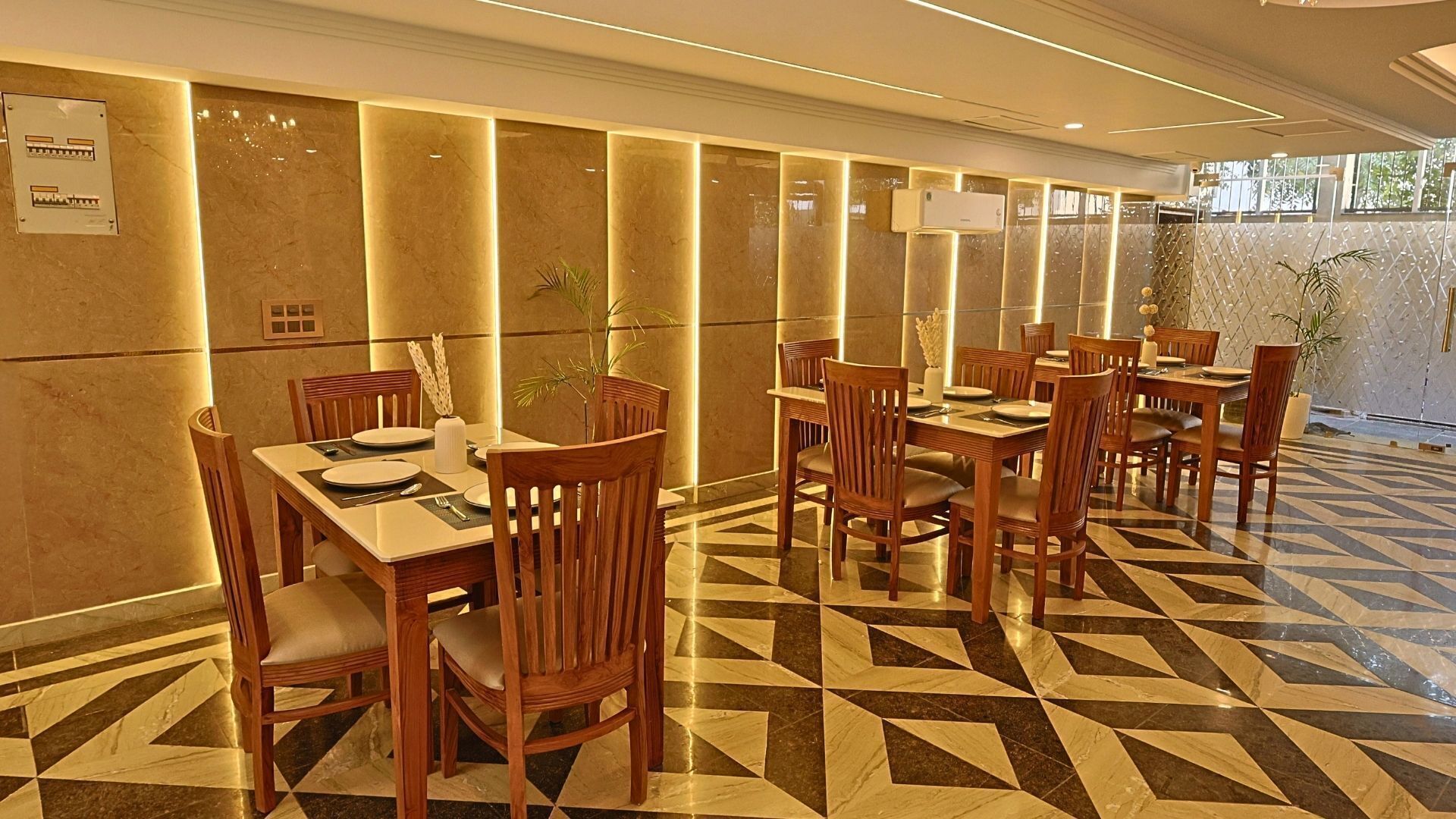 A hotel dining area with wooden tables and chairs, a patterned floor, and a wall-mounted air conditioning unit.