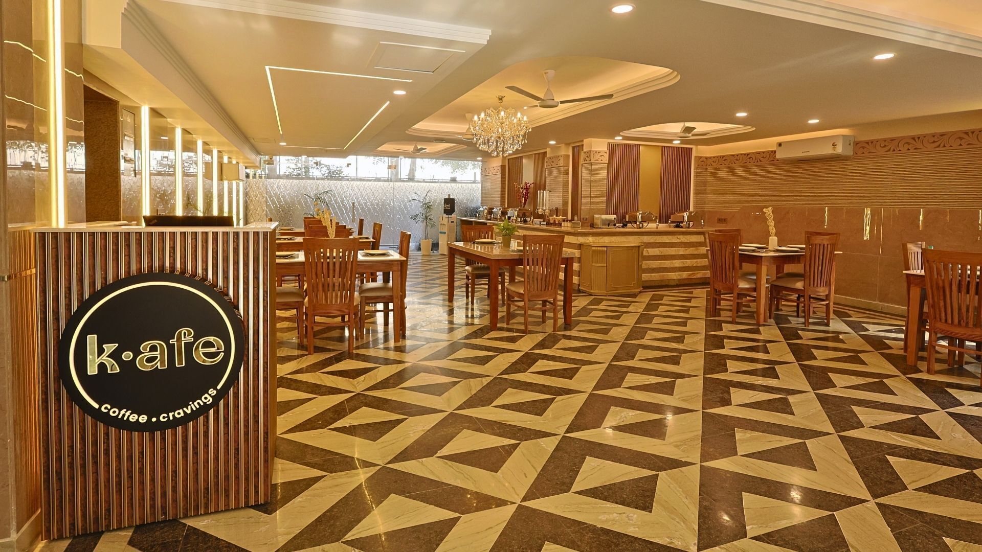 Una cafetería con piso de diseño geométrico, mobiliario de madera y un letrero que dice 'kafe coffee cravings'.