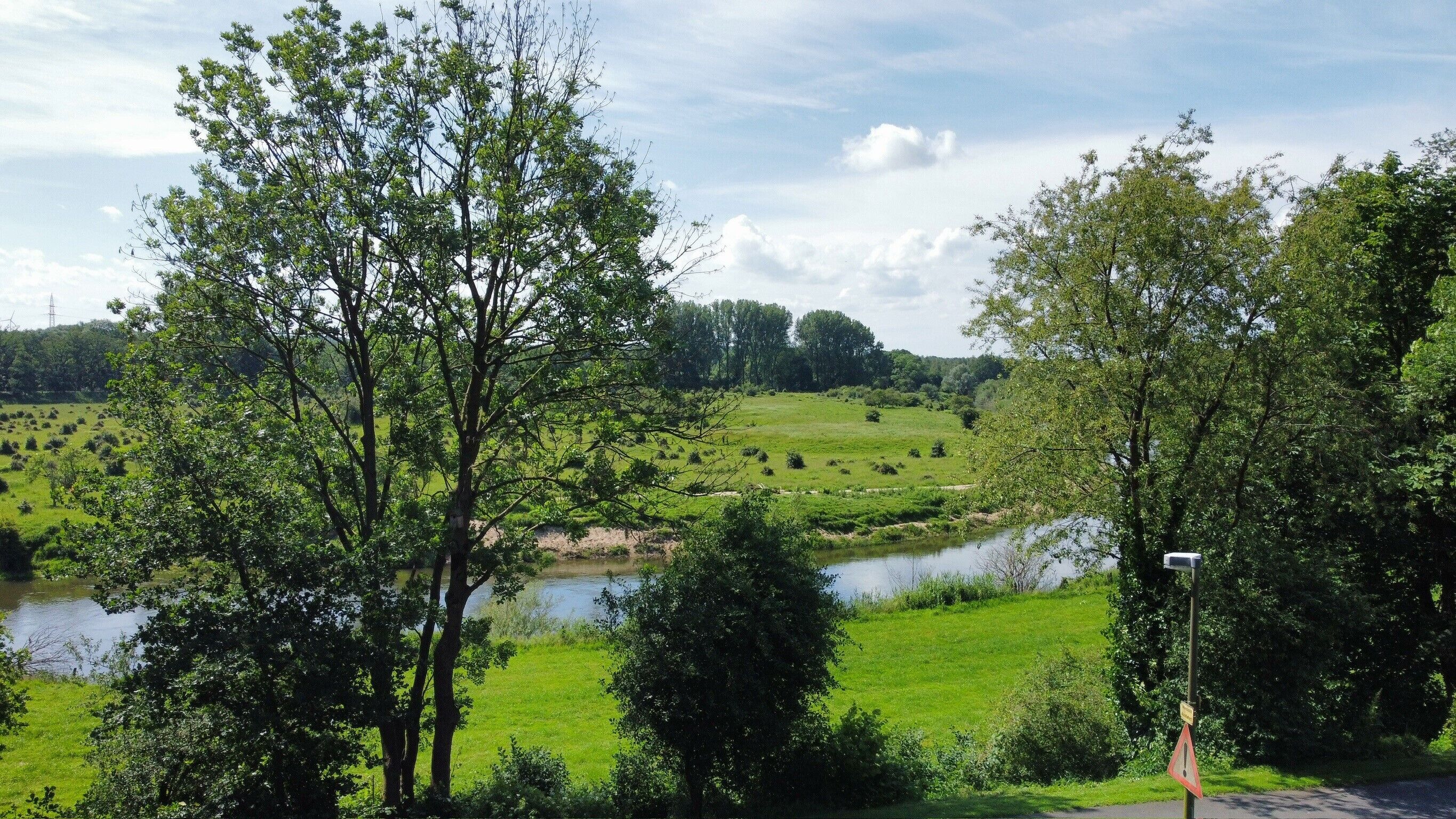 Een landelijk landschap met een rivier, bomen en een grasveld.