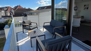 A balcony with outdoor furniture, a glass door leading to an interior space, and a view of neighboring houses.