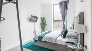 Une chambre moderne avec un lit, une télévision, une plante et une fenêtre avec des rideaux.