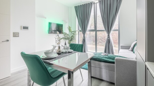 Un salon moderne comprenant un coin repas, un canapé gris, un fauteuil vert et un téléviseur fixé au mur.