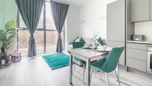 Une cuisine moderne avec un coin repas, de grandes fenêtres avec des rideaux, un tapis turquoise et une plante en pot.
