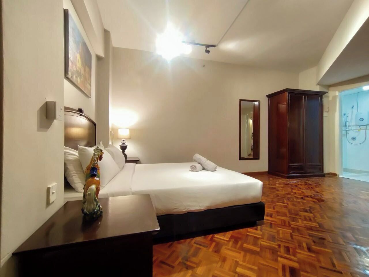 Una habitación de hotel con cama, mesita de noche, espejo, armario y suelo de madera.