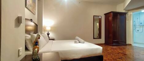 Una habitación de hotel con cama, mesita de noche, espejo, armario y suelo de madera.
