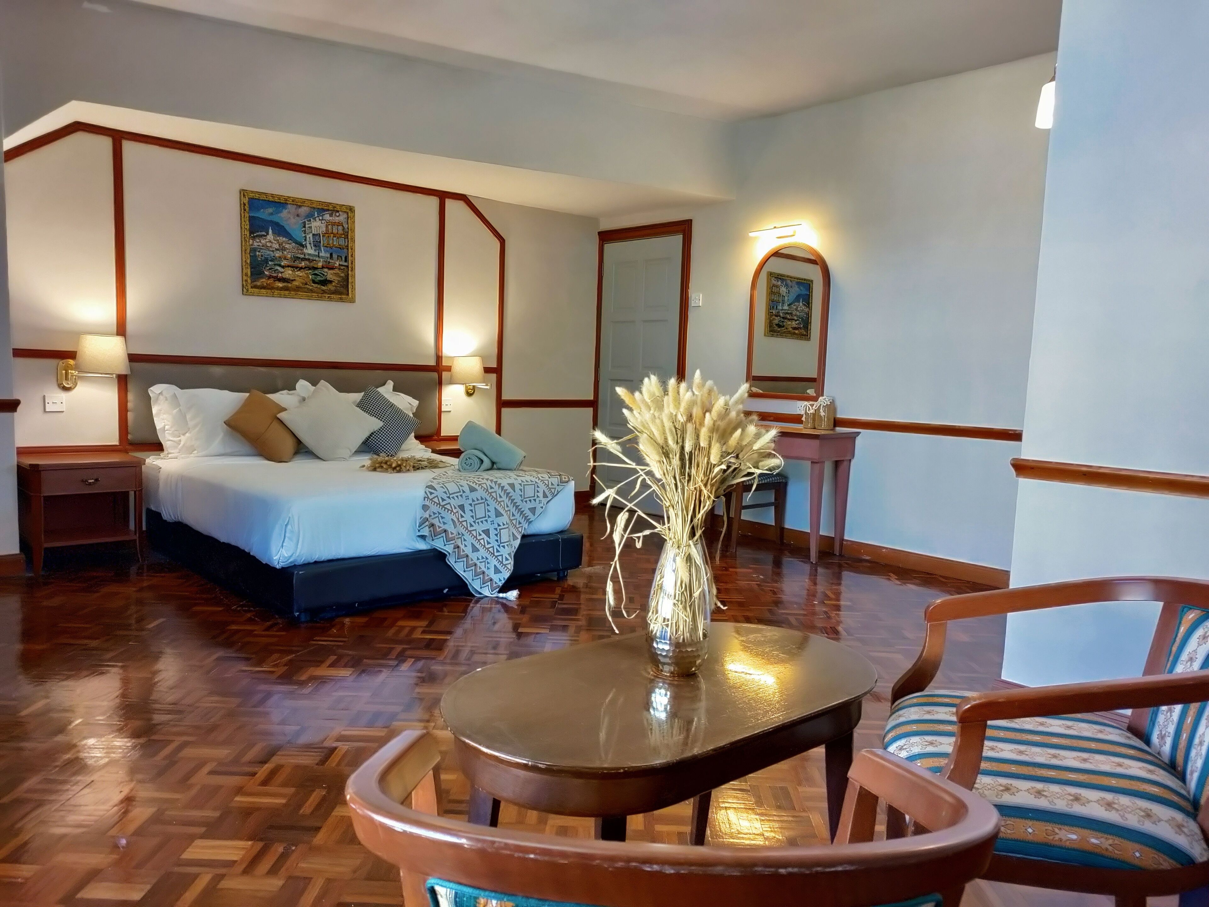 A hotel room with a bed, bedside tables, a small table with a vase, a chair, and a mirror.