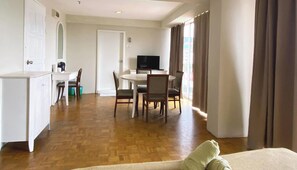Ein Hotelzimmer mit Holzboden, einem Essbereich mit Tisch und Stühlen, einem Fernseher und einem Bett mit Kissen.