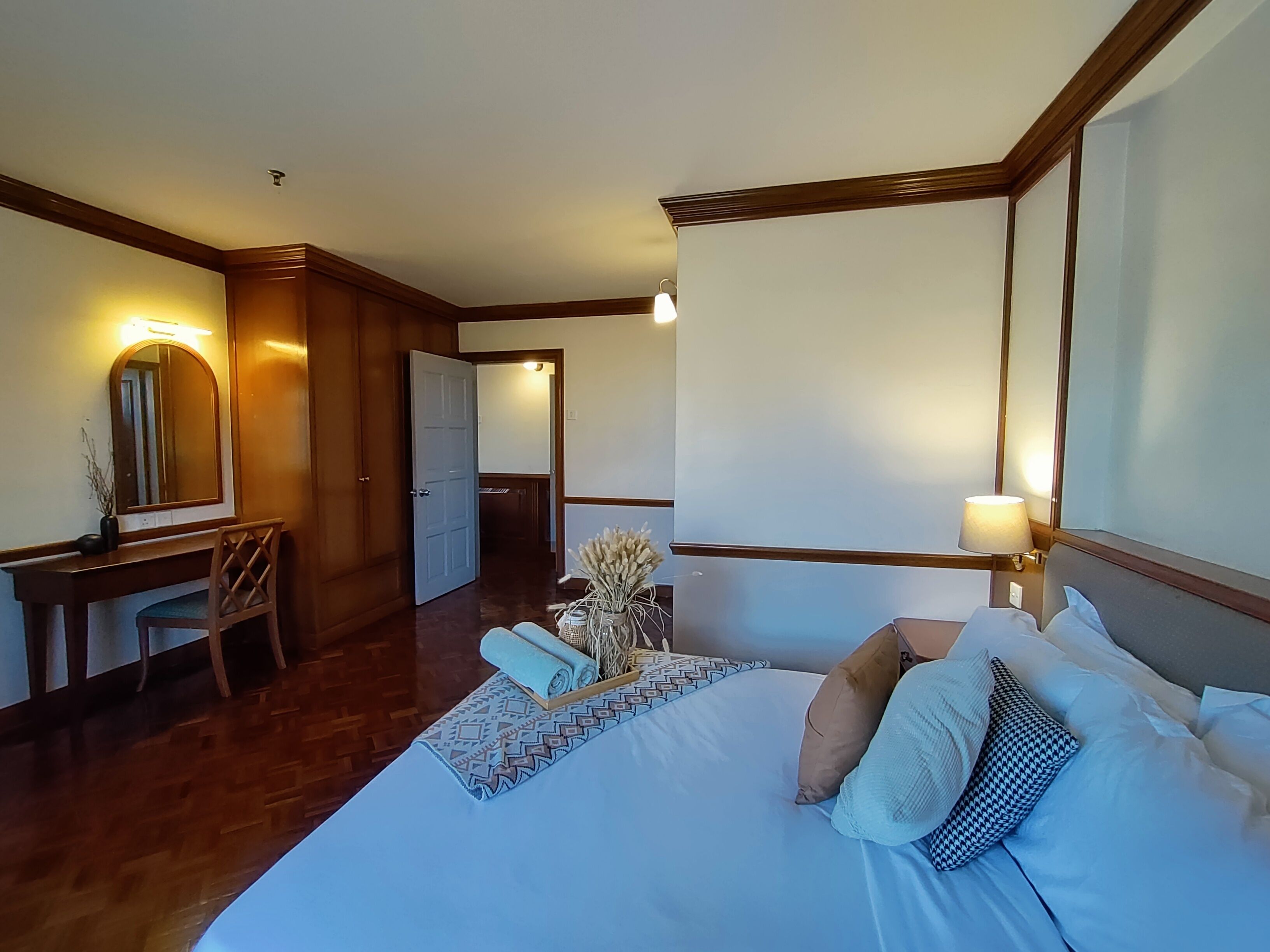 Una camera d'albergo con un letto grande, una scrivania con una sedia, uno specchio e un comodino con una lampada.