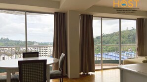 Habitación de hotel con comedor, ventanas amplias con cortinas y vistas a la ciudad y colinas.