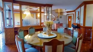 Un comedor con una mesa redonda de vidrio, seis sillas y un florero con flores secas.