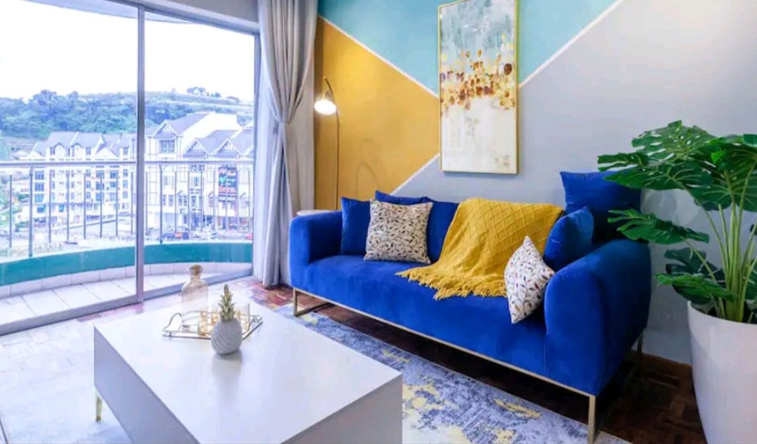 Ein modernes Wohnzimmer mit einem blauen Sofa, einem gelben Überwurf und einem großen Fenster mit Blick auf die Stadt.