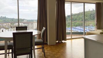 Habitación de hotel con comedor, ventanas amplias con cortinas y vistas a la ciudad y colinas.