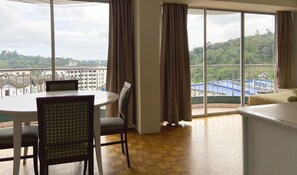 Habitación de hotel con comedor, ventanas amplias con cortinas y vistas a la ciudad y colinas.