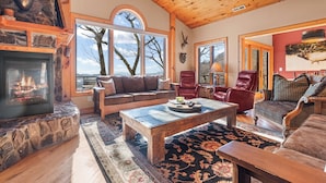 Una sala de estar acogedora con chimenea de piedra, ventanas amplias y vistas al exterior.