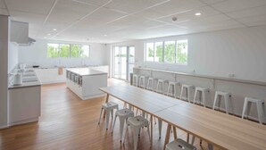 A spacious kitchen with a long dining table and stools, large windows, and a clean, modern design. - Bounce Airlie Beach (Airlie Beach)