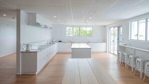 A modern kitchen with white cabinetry, a central island, bar stools, and large windows. - Bounce Airlie Beach (Airlie Beach)