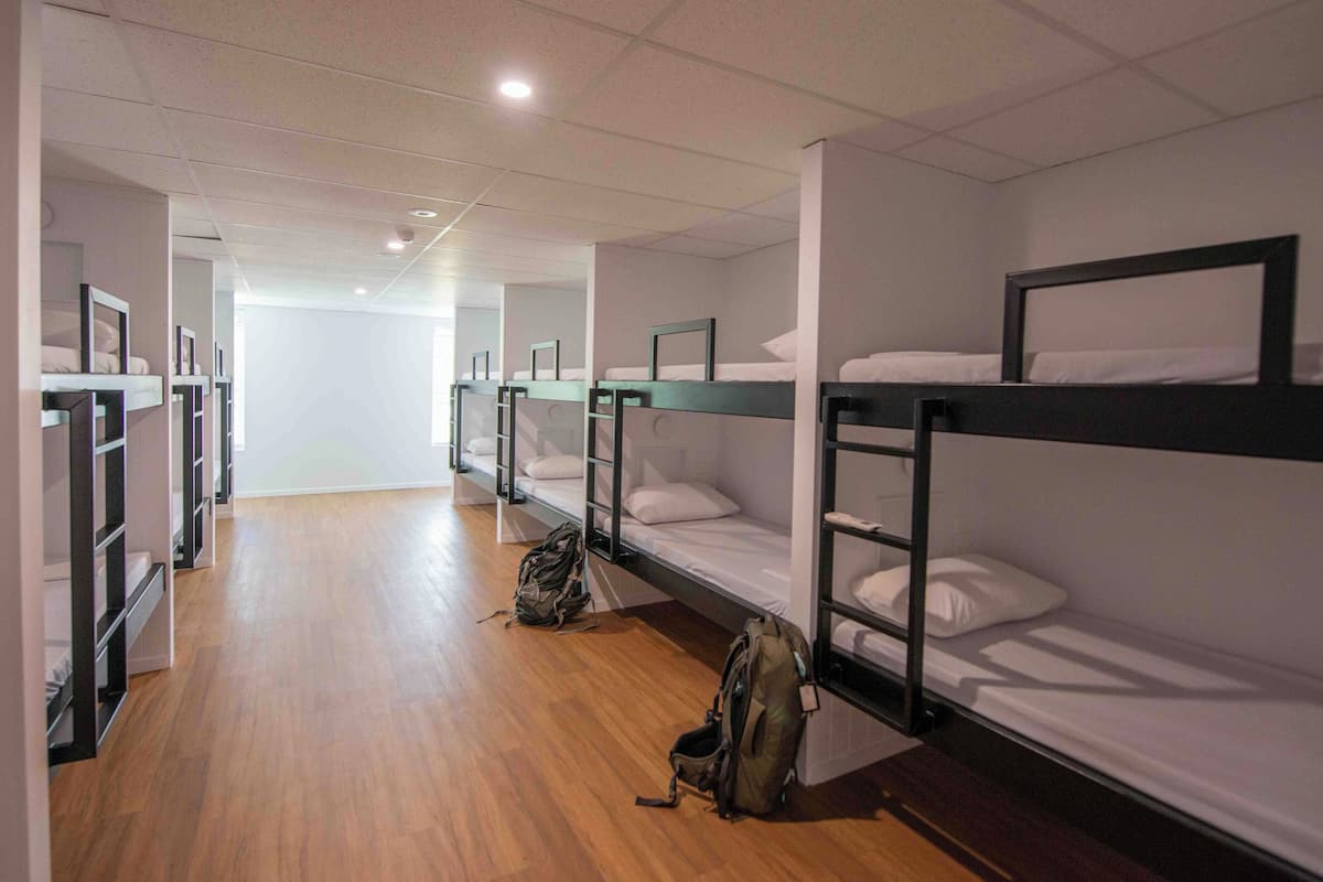 Ein Schlafsaalzimmer mit Etagenbetten, Holzböden und einem Rucksack auf dem Boden.