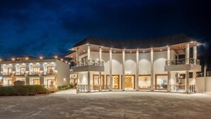 A multi-story hotel with a central courtyard, balconies, and a well-lit facade. - Shervani Pebbles And Pine, Corbett (Ramnagar)