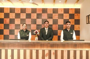 A reception desk with three staff members, a checkered wall, and a ceiling fan. - Shervani Pebbles And Pine, Corbett (Ramnagar)