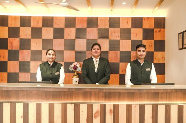 A reception desk with three staff members, a checkered wall, and a ceiling fan. - Shervani Pebbles And Pine, Corbett (Ramnagar)