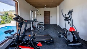 A modern gym with cardio equipment, a weight bench, and a treadmill. - Shervani Pebbles And Pine, Corbett (Ramnagar)