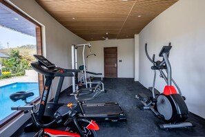 A modern gym with cardio equipment, a weight bench, and a treadmill. - Shervani Pebbles And Pine, Corbett (Ramnagar)