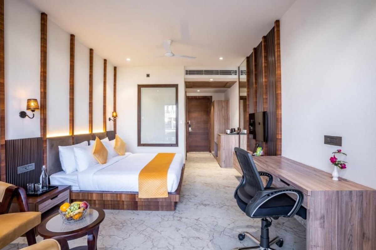 A modern hotel room with a bed, desk, chair, and a small table with fruit.