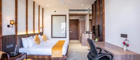 A modern hotel room with a bed, desk, chair, and a small table with fruit.