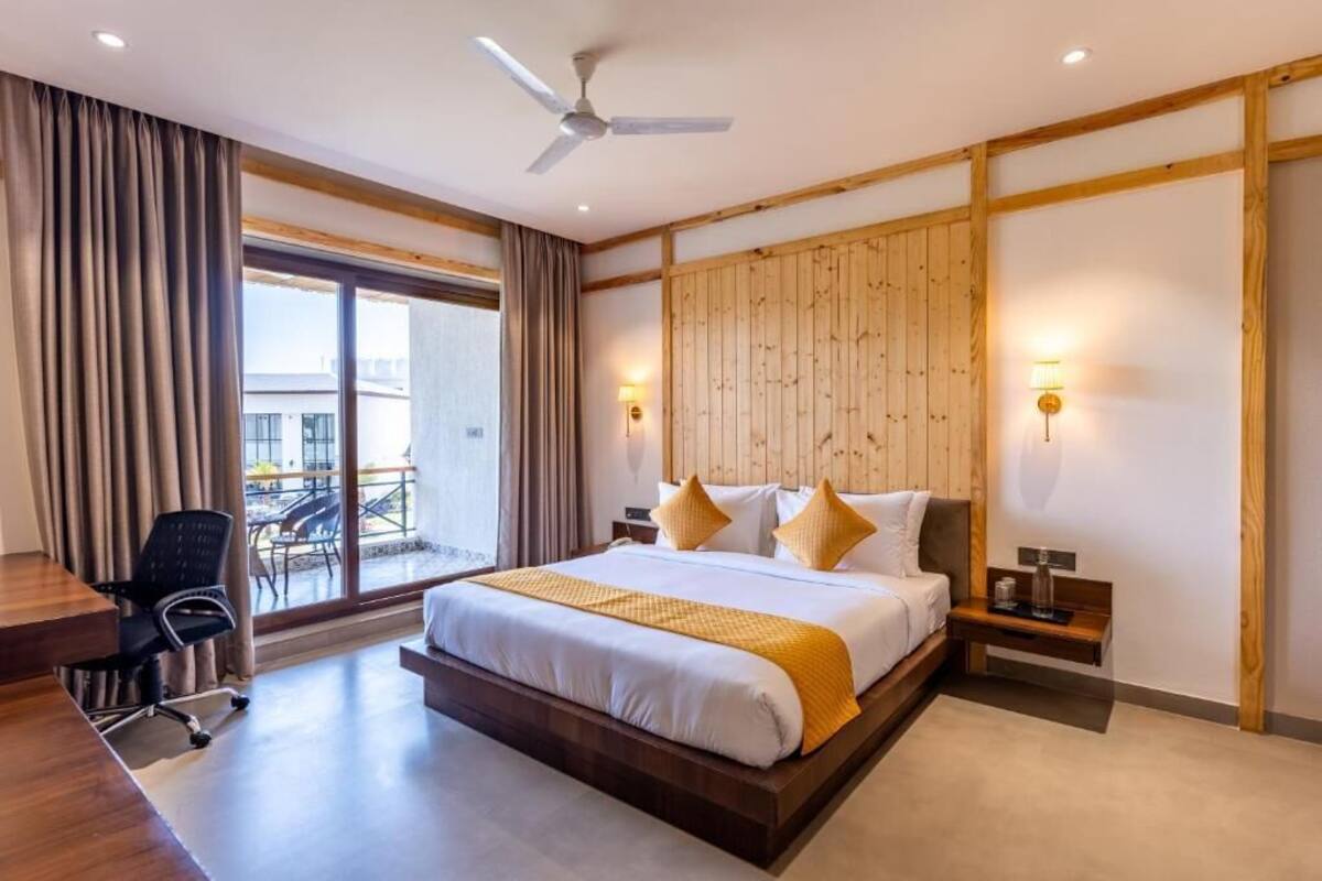A hotel room with a large bed, a desk, and a chair. There is a balcony with a table and chairs outside the window.
