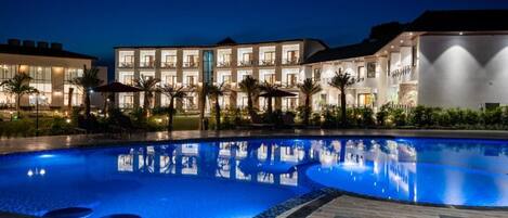 A swimming pool with a reflection of the hotel buildings at night.