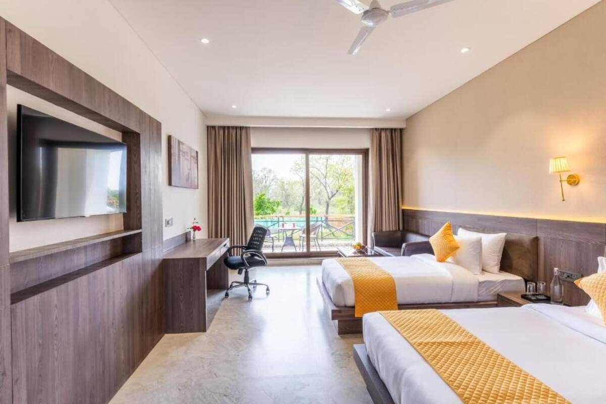 A hotel room with two beds, a desk, a chair, a TV, and a balcony with a view.