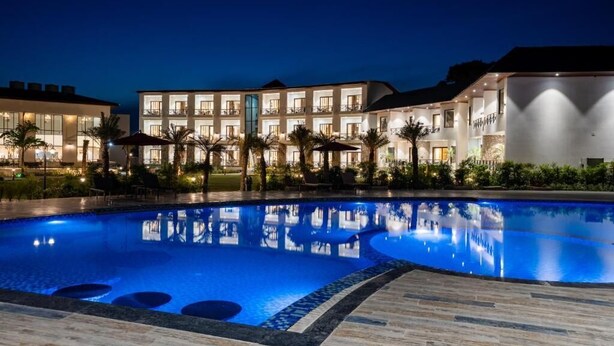 A swimming pool with a reflection of the hotel buildings at night. - Shervani Pebbles And Pine, Corbett (Ramnagar)