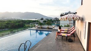 A rooftop pool area with a view of the mountains, a lounge with striped cushions, and a table with a chair. - Hotel Bawa Udaipur (Udaipur)