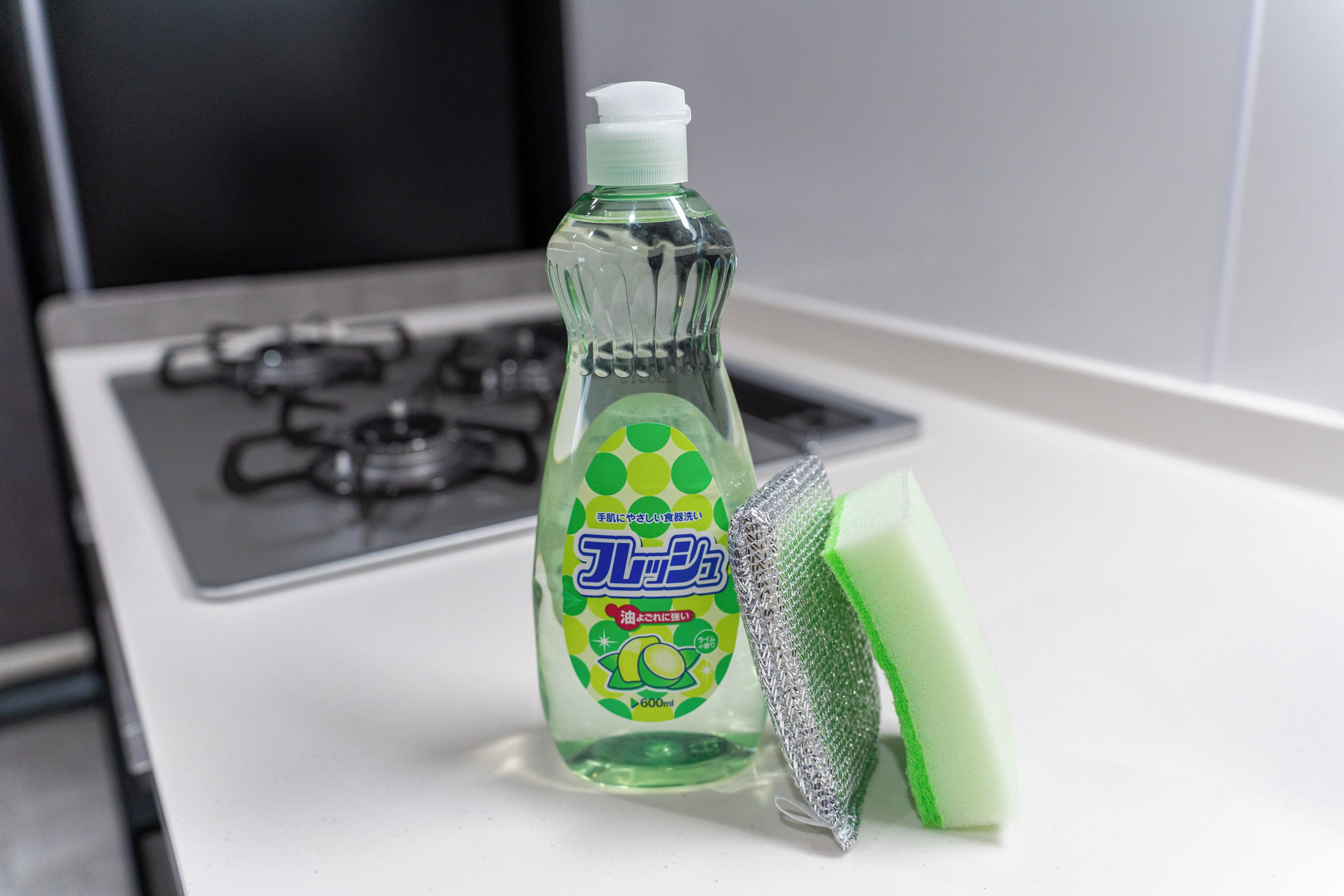 A bottle of dish soap and a green sponge on a white countertop.