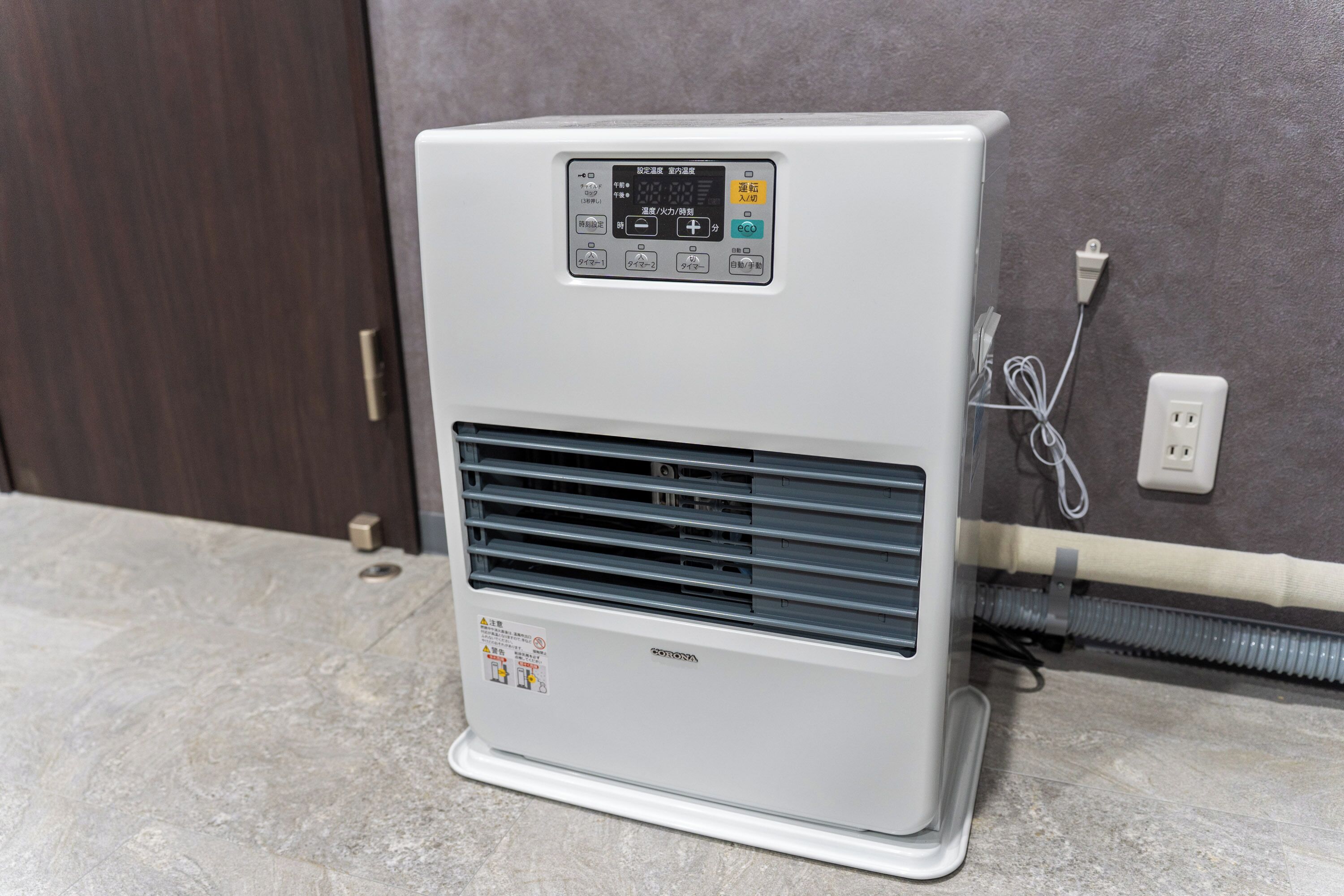 A portable air conditioner with a digital display, placed on a tiled floor next to a wall socket.