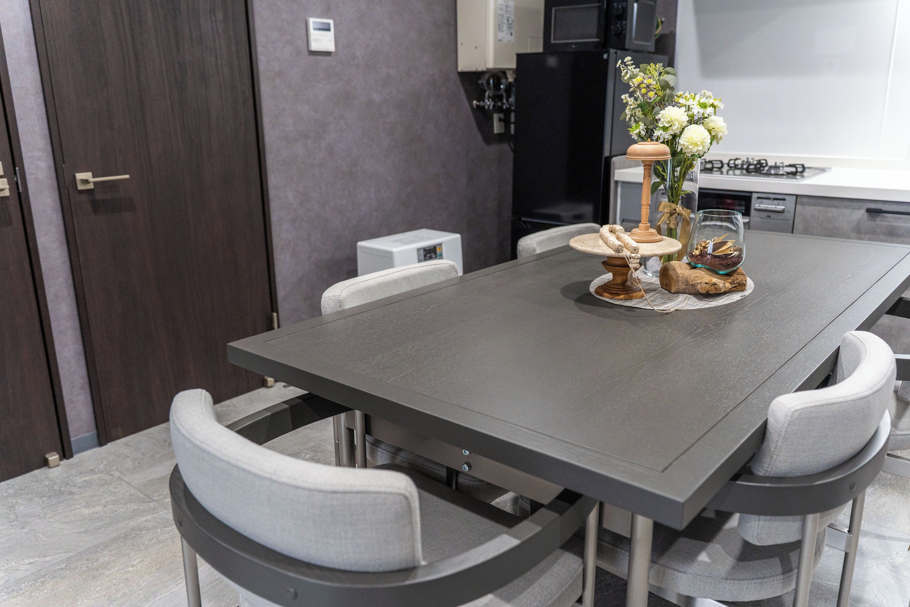 A modern kitchen with a dark grey table, white chairs, and a small refrigerator.