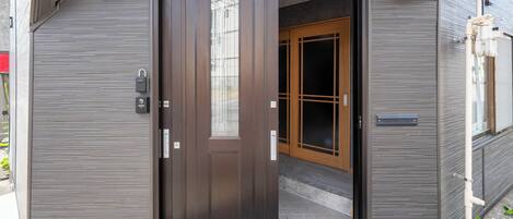 Entrada de un edificio moderno con puerta corredera, una puerta de madera y un pequeño ventanal sobre la puerta corredera.
