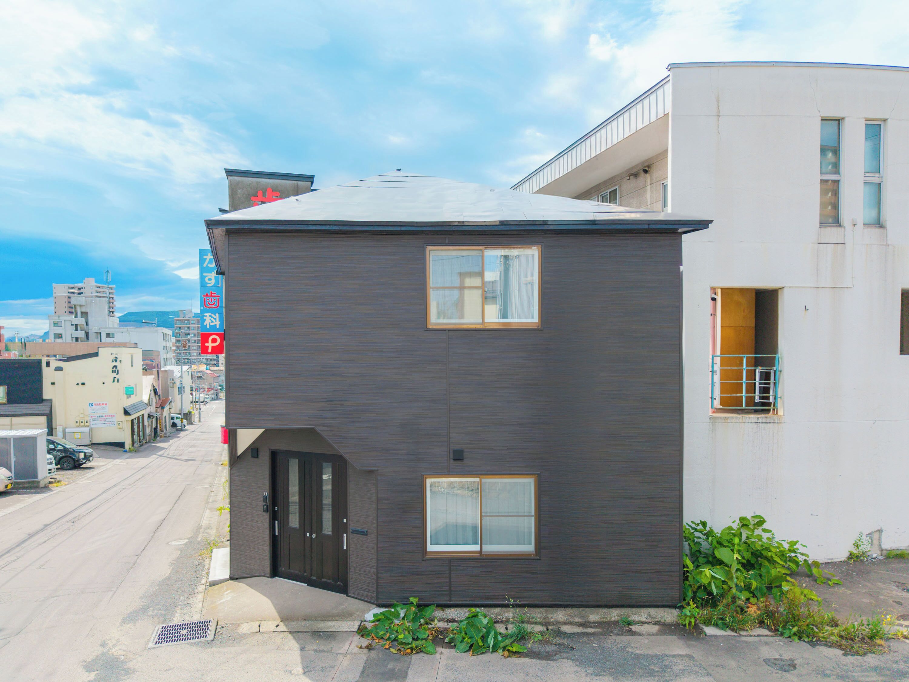 A modern two-story building with a dark facade, a small entrance, and two windows on the ground floor.