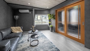Un espace d’attente moderne, avec un canapé en cuir, une petite table ornée d’un vase et une grande fenêtre donnant sur la rue.