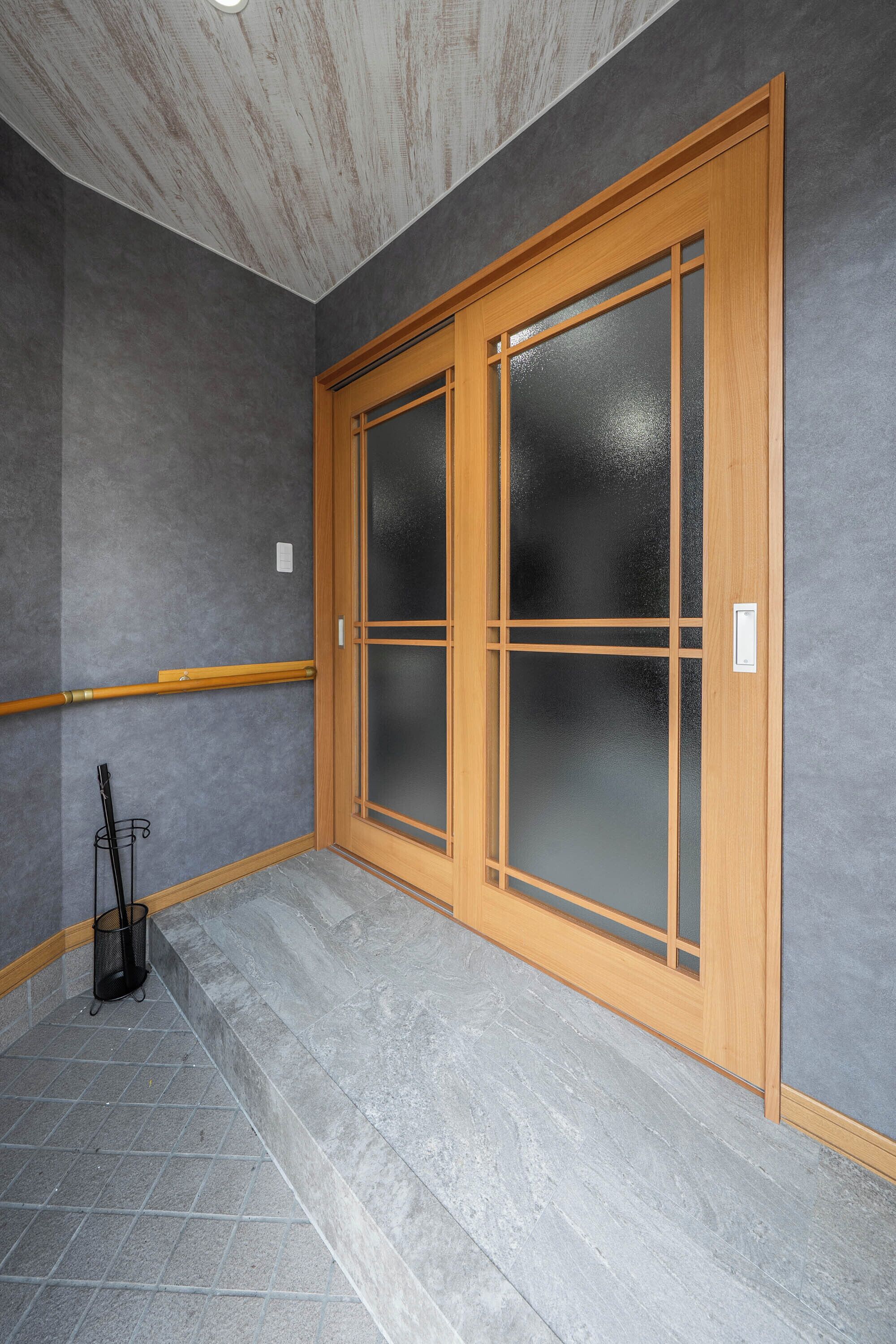 A room with grey walls, a wooden door with frosted glass panels, and a grey tiled floor.
