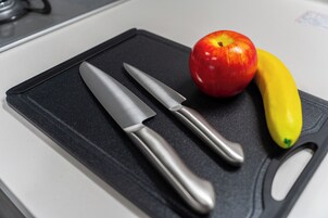 Una encimera de cocina con una tabla de cortar negra, dos cuchillos, una manzana roja y un plátano amarillo.