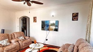 Een woonkamer met een plafondventilator, een flatscreen televisie, twee banken, een salontafel en een vloerkleed met een patroon.