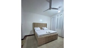 Een slaapkamer met een bed, een plafondventilator en een raam met gordijnen.