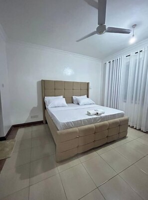 Une chambre à coucher avec un lit, un ventilateur de plafond et une fenêtre avec des rideaux.